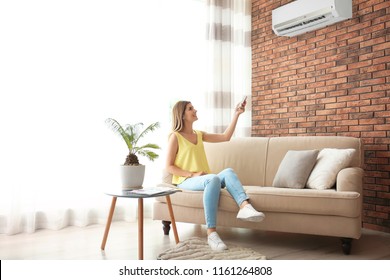 Woman operating air conditioner while sitting on sofa at home - Shutterstock ID 1161264808