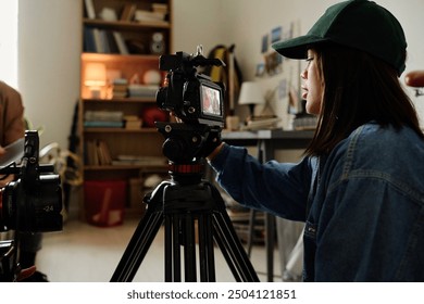 Woman operating professional video camera on tripod, capturing scene in indoor setting with bookshelves and equipment visible in background - Powered by Shutterstock