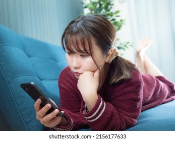 ソファーの上に横になったスマートフォンを操作する女性