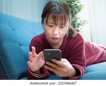 ソファーの上に横になったスマートフォンを操作する女性