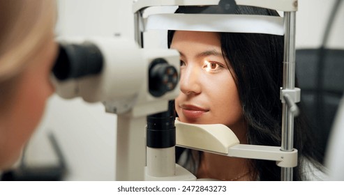 Woman, optometry and slit lamp in clinic for test, vision or exam for wellness assessment with health. Doctor, optician and patient by machine, light and laser for retina scan with lens for eye care - Powered by Shutterstock