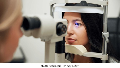 Woman, optometry and slit lamp for test, vision or care for wellness assessment with health in clinic. Doctor, optician and patient by machine, light and laser for retina scan with lens for eye exam - Powered by Shutterstock