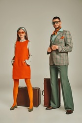 Woman In Orange Dress And Sunglasses Near Happy Man In Plaid Blazer And Vintage Suitcases On Grey