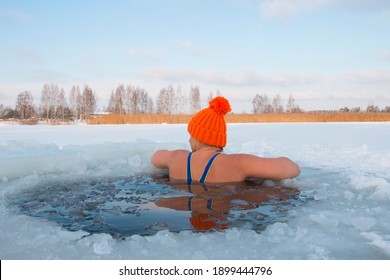 woman in an orange hat bathes in an ice-hole in winter, extreme swimming at -15 frost