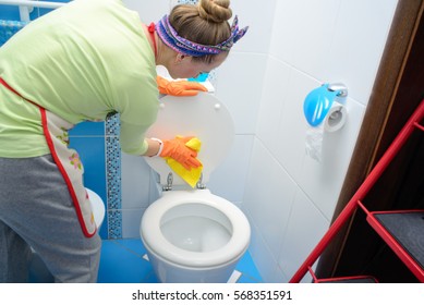 Woman in orange rubber gloves cleaning toilet with pink cloth