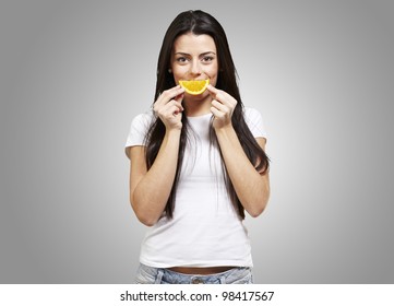 Woman With An Orange Slice As A Smile Against A Grey Background