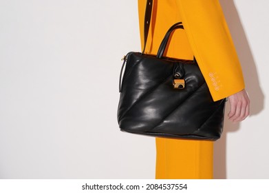 Woman In An Orange Suit With Black Leather Handbag In Her Hand On The White Background. Quilted Tote Bag Stylish Accessory. New Collection Or Sale Background. Horizontal Photo With Copy Space. Closeup