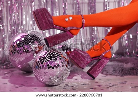 Woman in orange tights and pink high heeled shoes among disco balls indoors, closeup