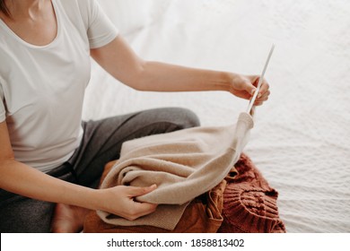 Woman Organizing Fall And Winter Warm Clothing. Young Woman Folding Sweaters On White Bed. Folding Laundrey.