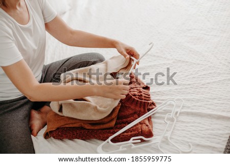 Woman organizing fall and winter warm clothing. Young woman folding sweaters on white bed. Folding laundrey.