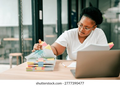 Woman organizing a large stack of color-coded documents and paperwork while working on a laptop