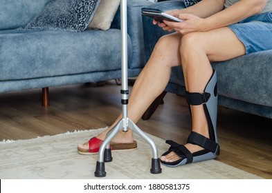 The woman with a orthotics on her foot is sitting on the sofa at home
