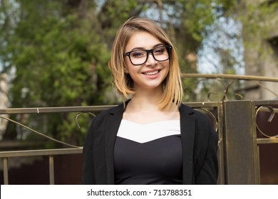 Woman Outdoors. Half Length Body Woman Girl Looking At You Camera Smile On Face, Black Suit Formal Wear, Eye Glasses Outside City Urban Home Fence On Background