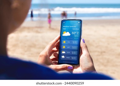 Woman outdoors on the beach checking the weather forecast on an app on her mobile phone. - Powered by Shutterstock