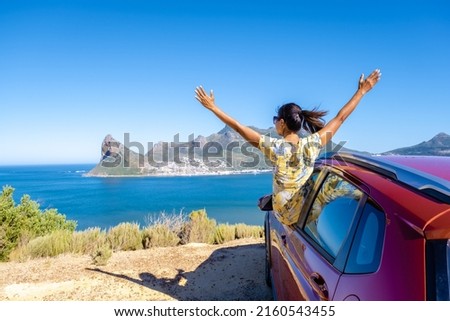 woman outside car window road trip with hands up, car at Chapmans Peak Drive in Cape Town South Africa looking out over the ocean. 