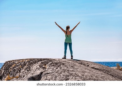 Woman with outstretched arms on a rocky peak by the sea - Powered by Shutterstock