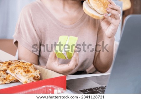 woman over eating fast food burger,  pizza and desserts at office desk, eating disorder concept 