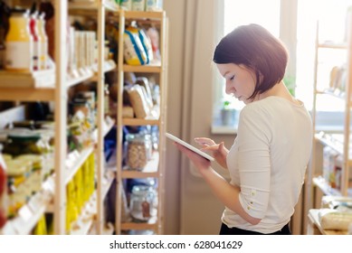 Woman Owner Of Small Local Grocery Store With Healthy Food Ordering Products Using A Tablet. Small Business Concept