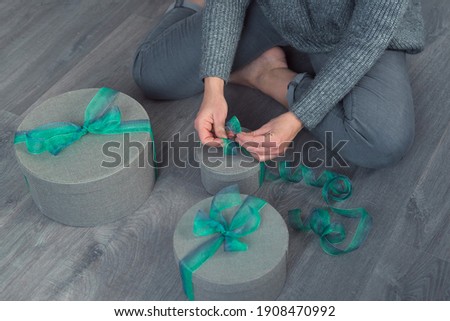 woman pack gifts with gray round boxes and green ribbon