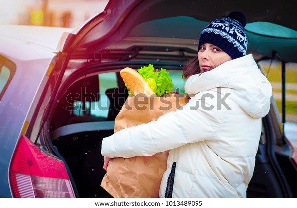 woman with package of food\
opened trunk of car in parking lot of supermarket. Shopping by car.\
Put shopping in trunk of car. Girl with paper product\
package