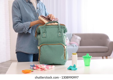 Woman Packing Baby Accessories Into Maternity Backpack On Table Indoors, Closeup