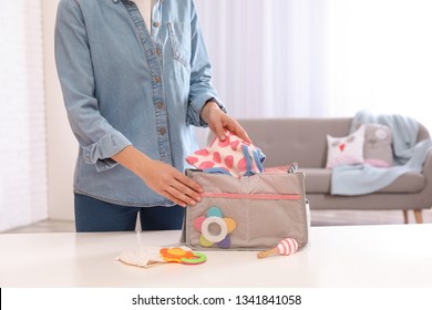 Woman Packing Baby Accessories Into Maternity Bag On Table Indoors, Closeup