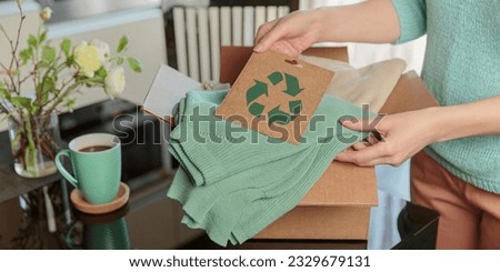 Woman packing box with used wardrobe and card with circular economy logo. Reusing, recycling materials and reducing waste in fashion, second hand apparel idea. Circular fashion, zero waste concept
