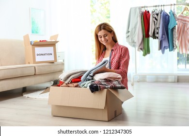 Woman Packing Clothes Into Donation Box In Living Room