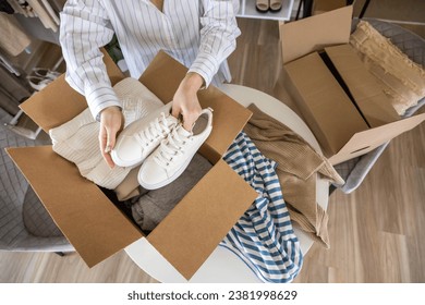 Woman packing clothes and shoes into cardboard box seasonal comfortable storage organize top view closeup. Female with container for wardrobe keep for donation charity online shopping order moving - Powered by Shutterstock