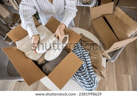 Woman packing clothes and shoes into cardboard box seasonal comfortable storage organize top view closeup. Female with container for wardrobe keep for donation charity online shopping order moving