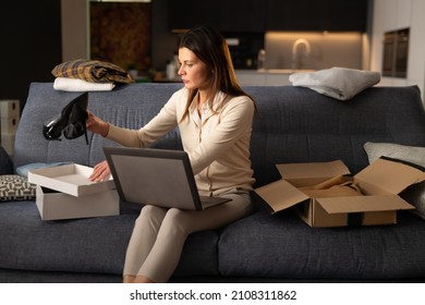 Woman is packing in mailing box used clothes and accessories from her wardrobe after decluttering and sorting it to sell with internet online marketplace app on laptop or donating to charity shop.