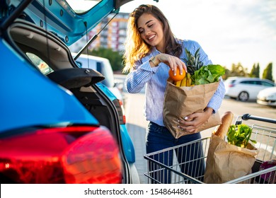 Woman packing shopping bags into a trunk of her car. Young woman with groceries at parking lot. Young women packing groceries from supermarket in car trunk. Woman holding groceries in reusable bag