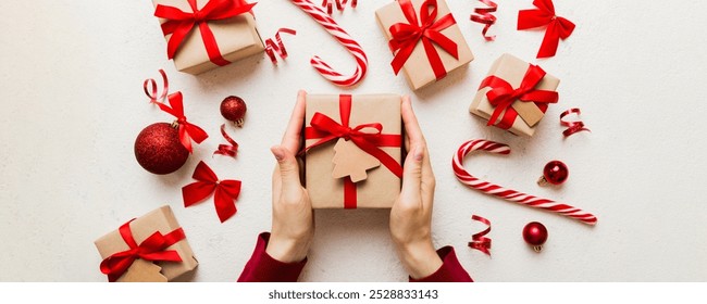 Woman is packing surprise gift for Christmas holidays, sitting at workplace with craft tools, top view. Woman wrapping Christmas gift at colored table. - Powered by Shutterstock