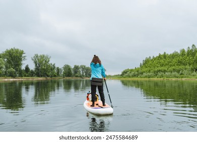 A woman paddleboards with her dog on a serene lake surrounded by lush greenery. Its a peaceful outdoor adventure in natures tranquility, perfect for relaxation and enjoying the tranquil setting - Powered by Shutterstock