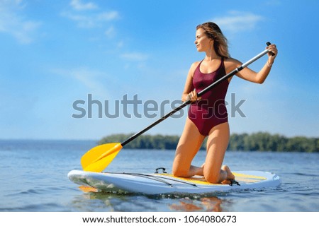 Woman paddling along the river standing on her knees on the sup board