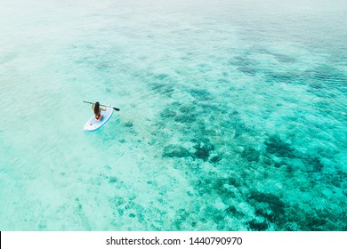 Woman paddling on sup board and enjoying turquoise transparent water and coral reef. Tropical travel, wanderlust and water activity concept. View from back.