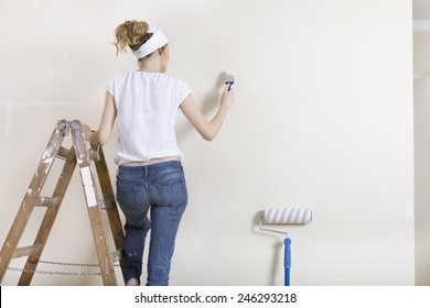 Woman With Paintbrush In Hand Standing On A Ladder And Painting A Wall