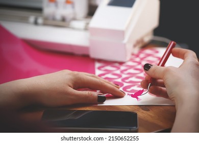 woman with painted nails weeds freshly cut peace dove stickers in pink color from carrier film. wooden worktop with plotting machine in background and mobile phone in forground. selective focus
 - Shutterstock ID 2150652255