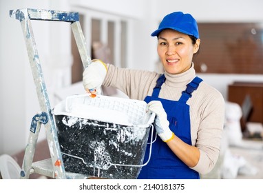 Woman Painter In Overalls With Paint Roller In A Building Under Construction