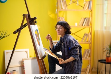 A woman painter is painting a modern artistic and abstract painting on a canvas and seems very cheerful as she is doing so - Powered by Shutterstock