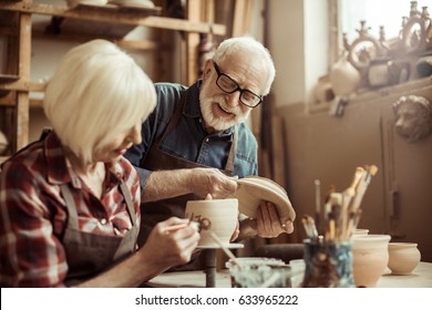 Woman Painting Clay Pot With Senior Potter At Workshop