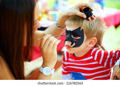 Woman Painting Face Of Kid Outdoors