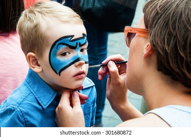 Woman Painting Face Of Kid Outdoors