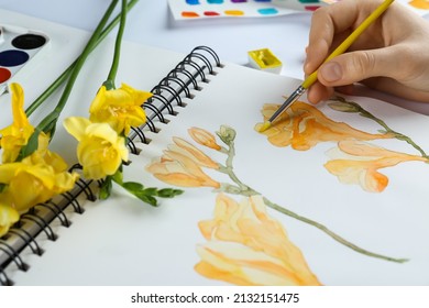 Woman painting freesias in sketchbook at white table, closeup