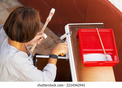 Woman Painting Furniture To Restore In Old Patio With Flowerpots And Whitewashed Walls , Selective Focus