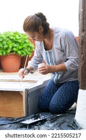 Woman Painting Furniture To Restore In Old Patio With Flowerpots And Whitewashed Walls