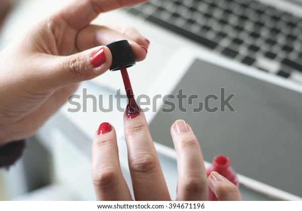 Woman painting her fingernails red, while\
working on the computer