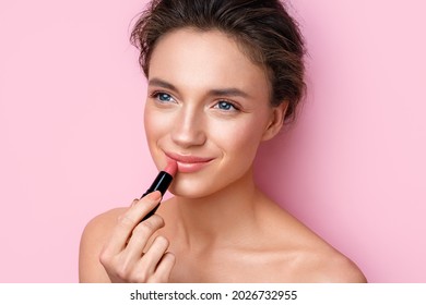 Woman Painting Her Lips With Beige Lipstick. Photo Of Woman With Perfect Makeup On Pink Background. Beauty Concept