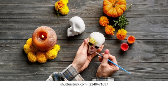 Woman Painting Human Skull On Dark Wooden Background, Top View. Mexico's Day Of The Dead (El Dia De Muertos)