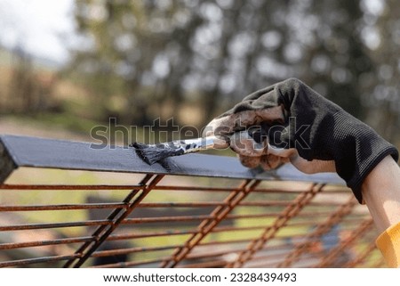 A woman is painting a metal grid with black paint outdoors